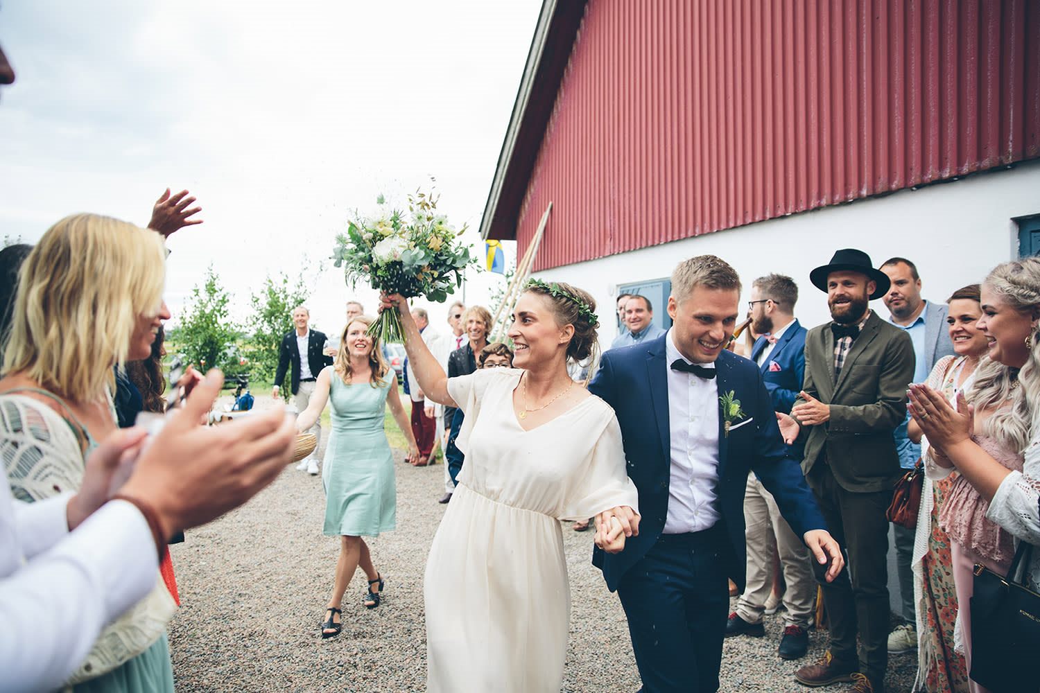 Nygift brudpar går hand i hand längs gårdsplanen medan gäster applåderar.