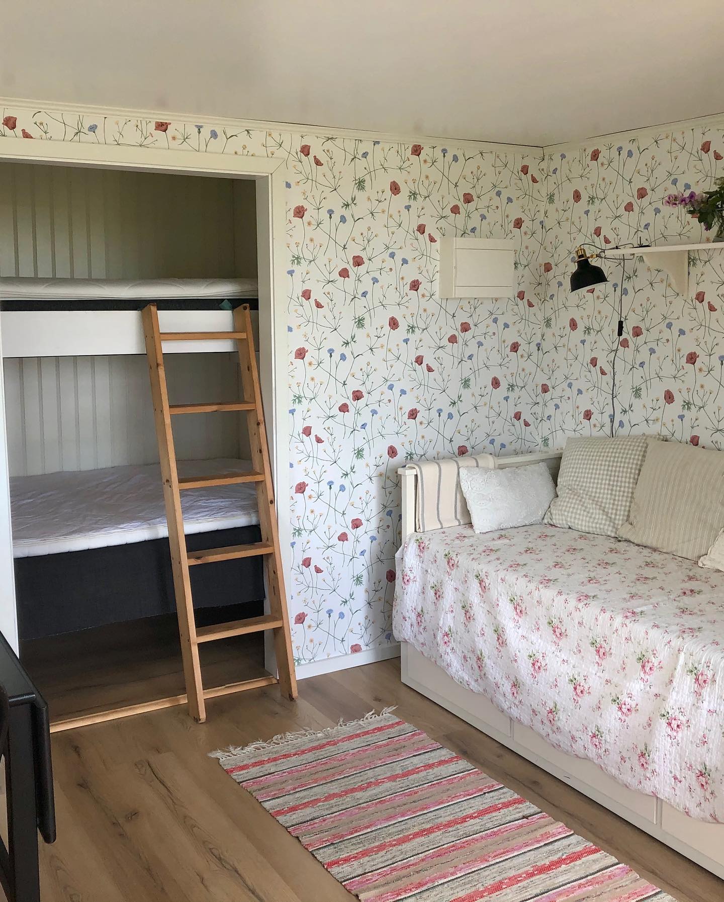 Rum i Sunnanvind med våningssäng i alkov och en ljus dagbädd med blommigt överkast.