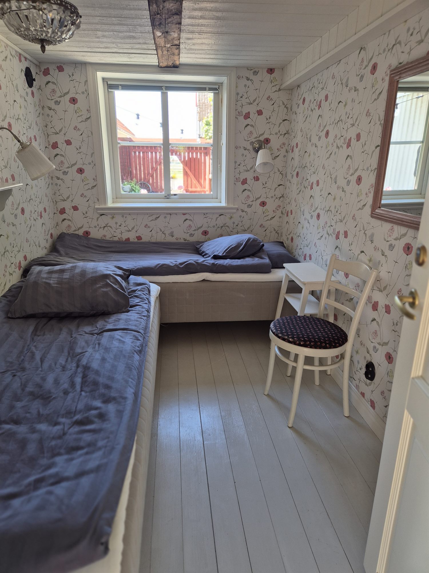 Litet sovrum i Gårdshuset med enkelsäng och fönster mot det röda staketet.