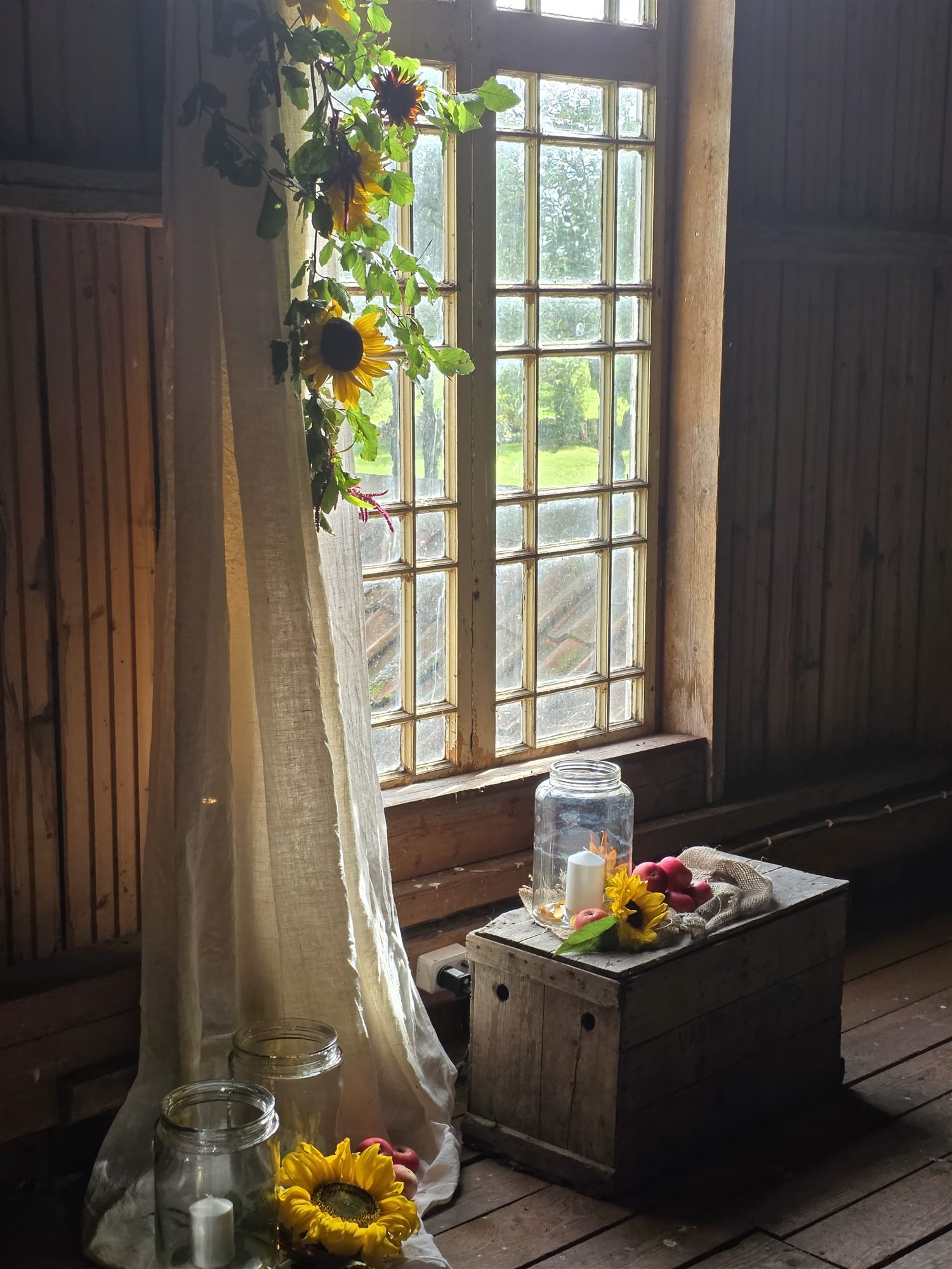 Det stora fönstret på loftet med en girlang av solrosor och en gammal låda med blommor.