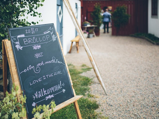 Griffeltavla som välkomnar bröllopsgäster vid grusgången mellan husen.