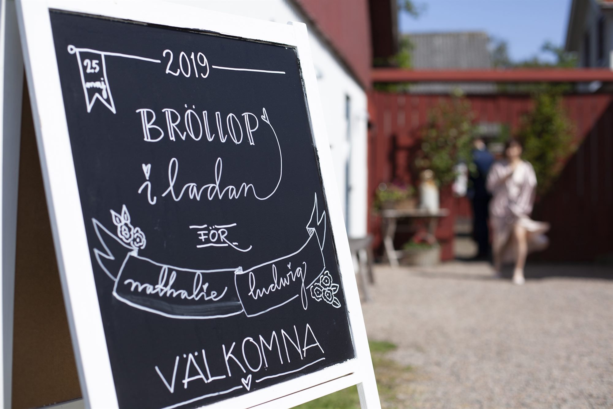 Griffeltavla med texten Bröllop i ladan och Välkomna, framför de faluröda husen.