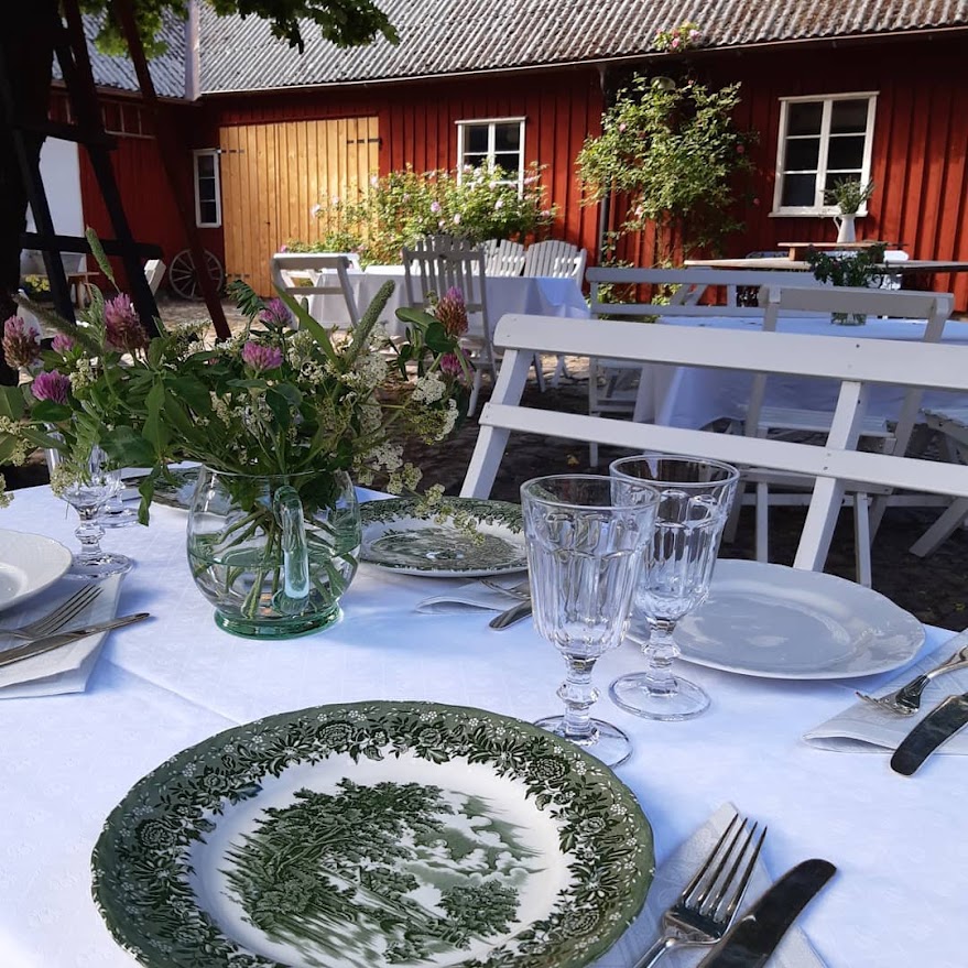 Enkelt dukade vita bord på innergården i Rönnås Lada, med vildblommor i vas och vita bänkar, inför en minnesstund.