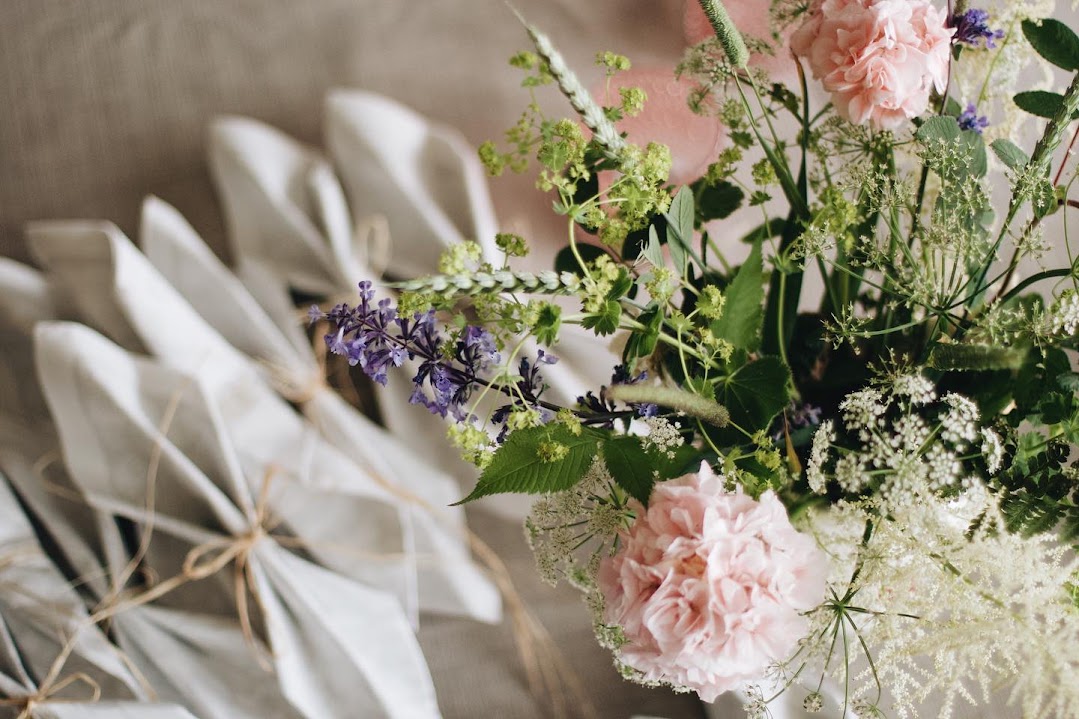 Vikta linneservetter bredvid en bukett med rosa nejlikor och ängsblommor.